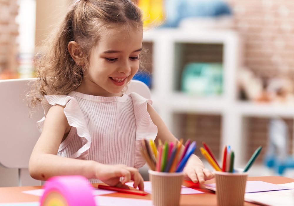 Adorable caucasian girl sitting on table drawing on paper at classroom