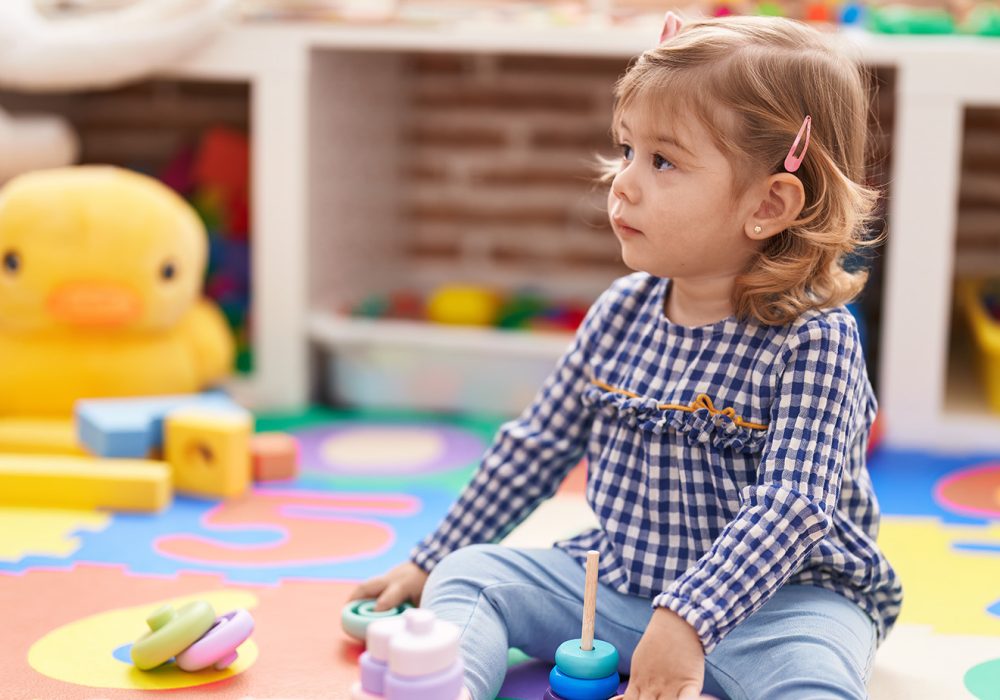 Adorable hispanic girl playing with hoops game sitting on floor at kindergarten